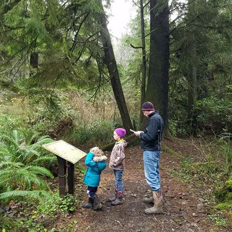 A dad and two children find clues on a sign on a forest trail
