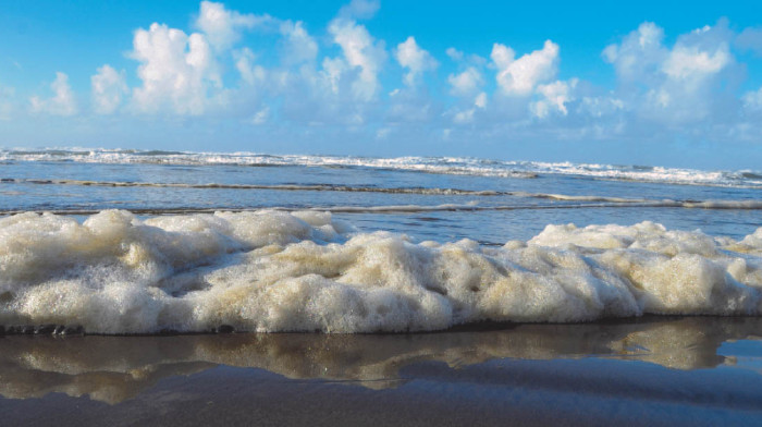 A line of fluffy sea foam sits along the waterline at the beach on a sunny day.