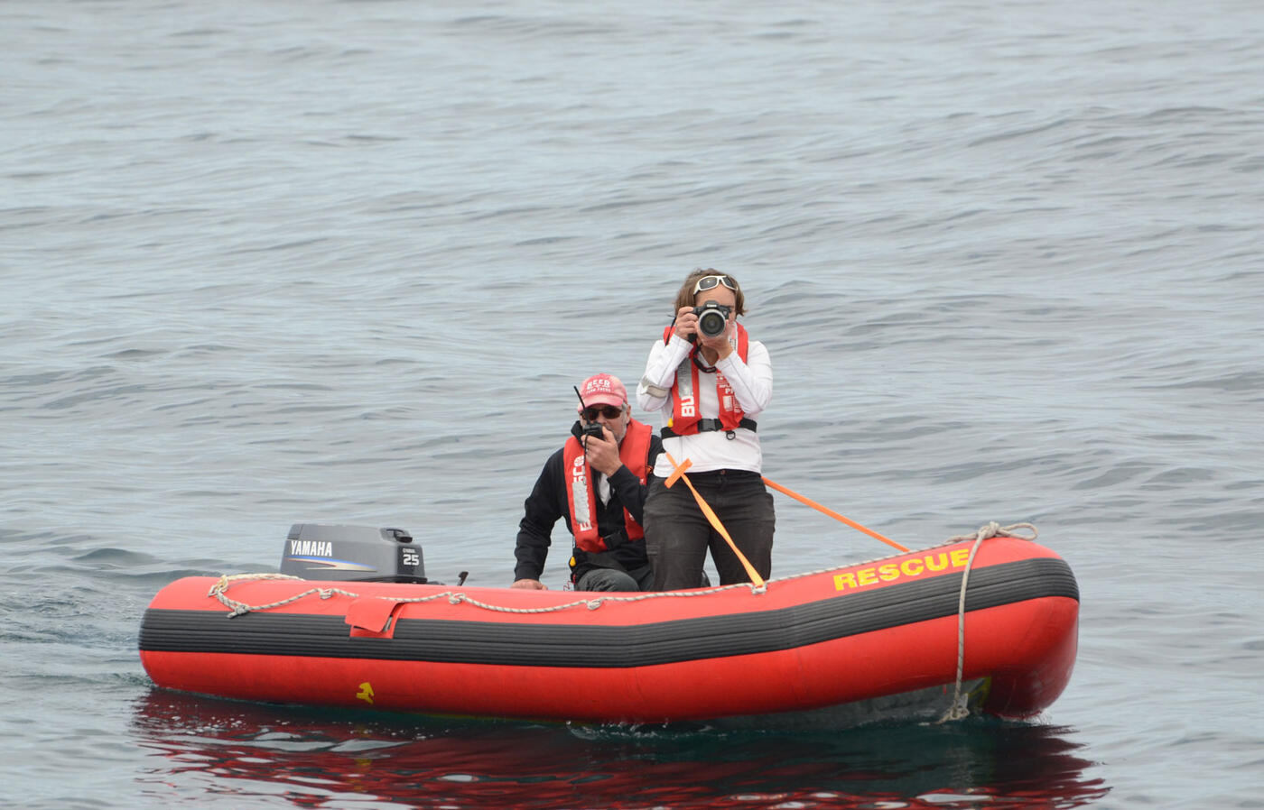 Two people in a dinghy floating on the water with one person taking pictures.