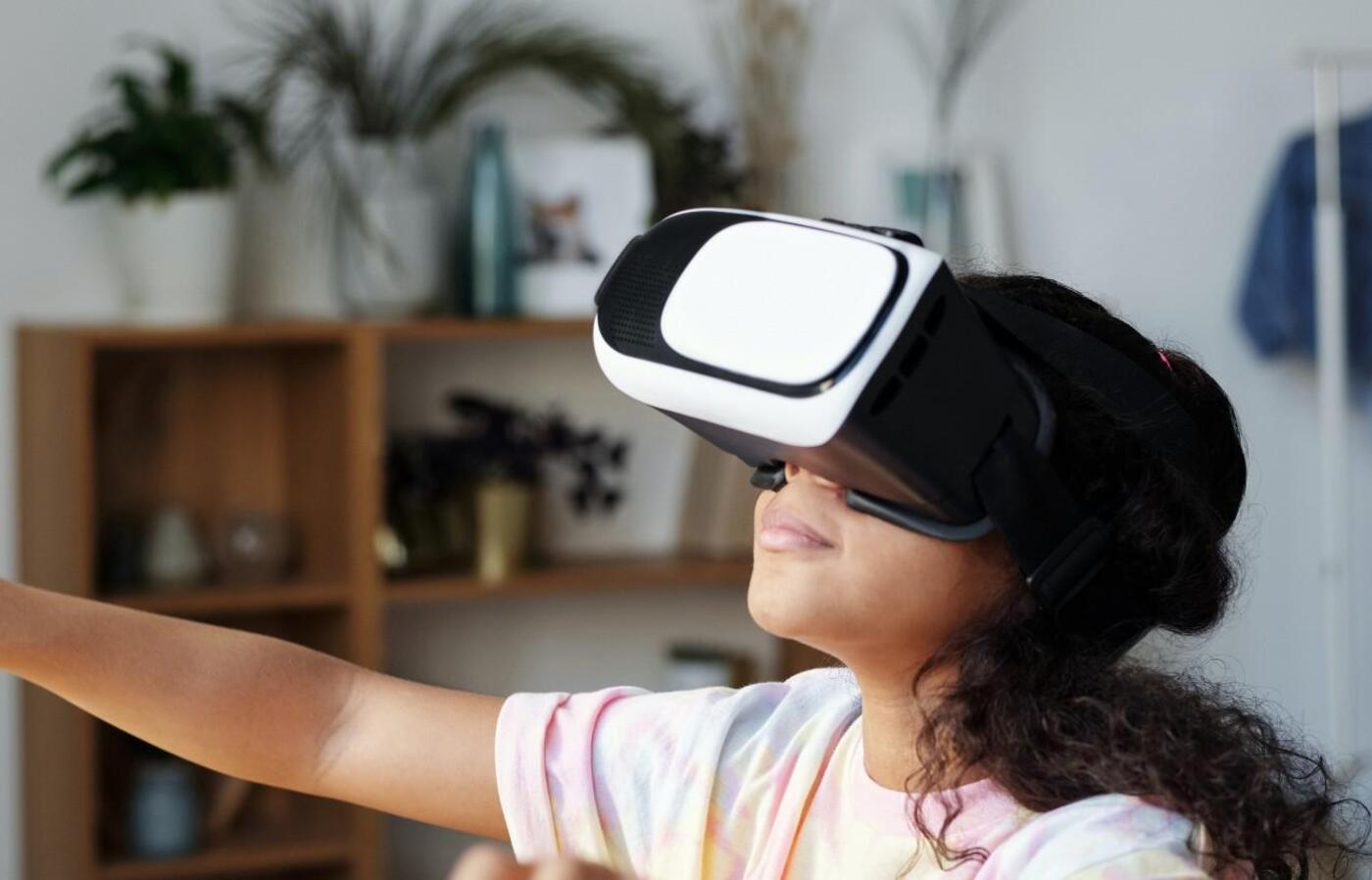 A girl in a room wears a virtual reality headset and has her arm outstretched