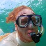 A man with red hair swims underwater with a snorkel.