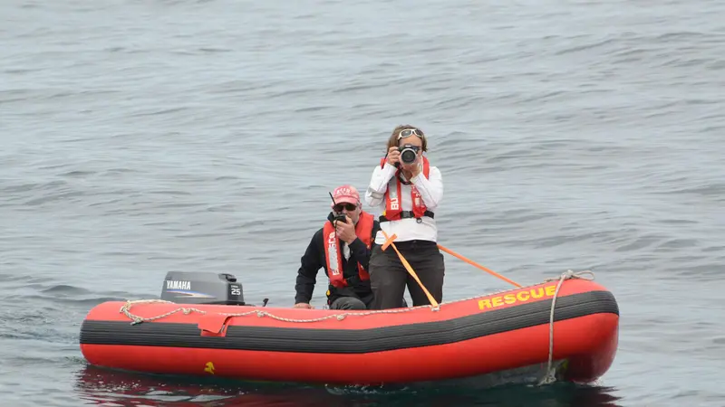 Two people in a dinghy floating on the water with one person taking pictures.