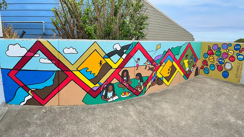 A colorful mural with blue sky and a tree behind it.