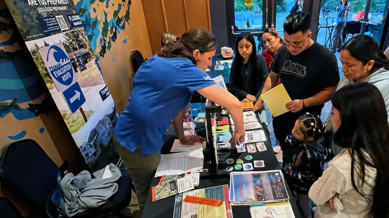 A group of people gather around a table with materials on it.