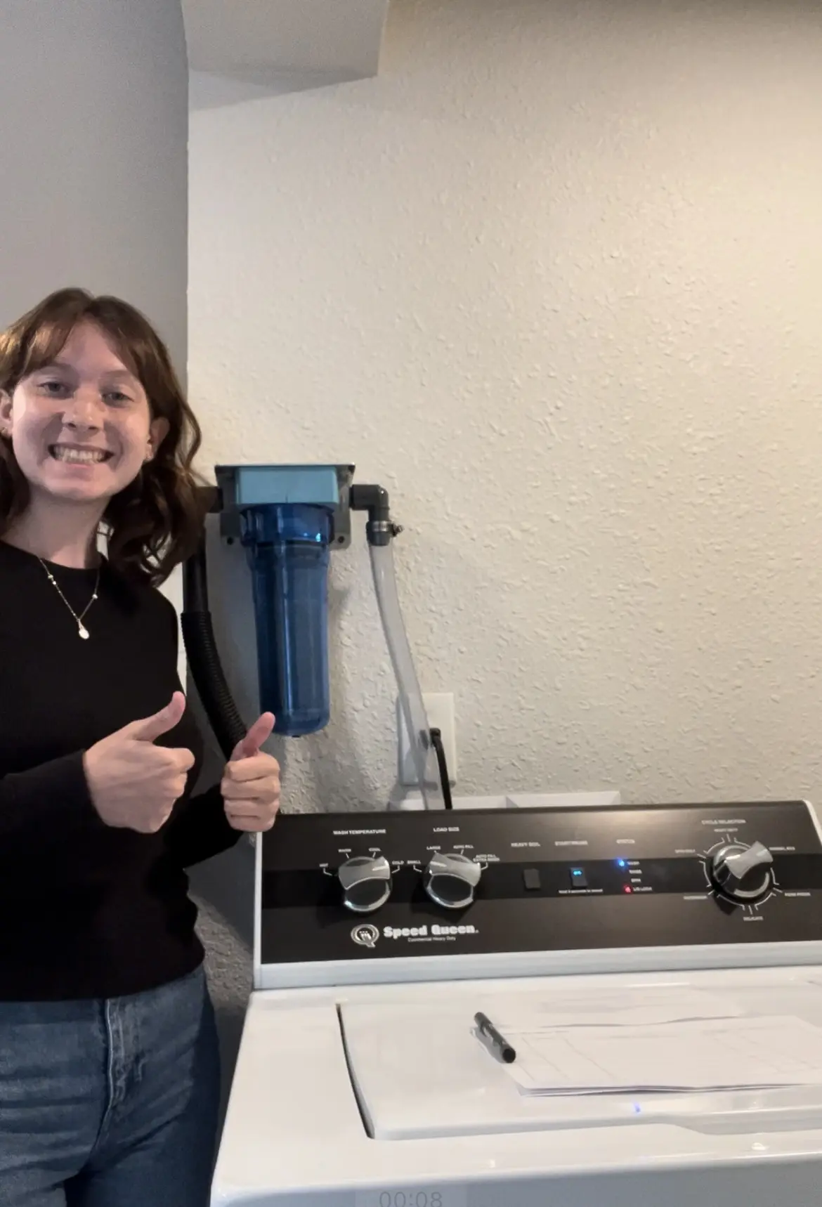 A person smiles at the camera with two thumbs up standing beside a washing machine.
