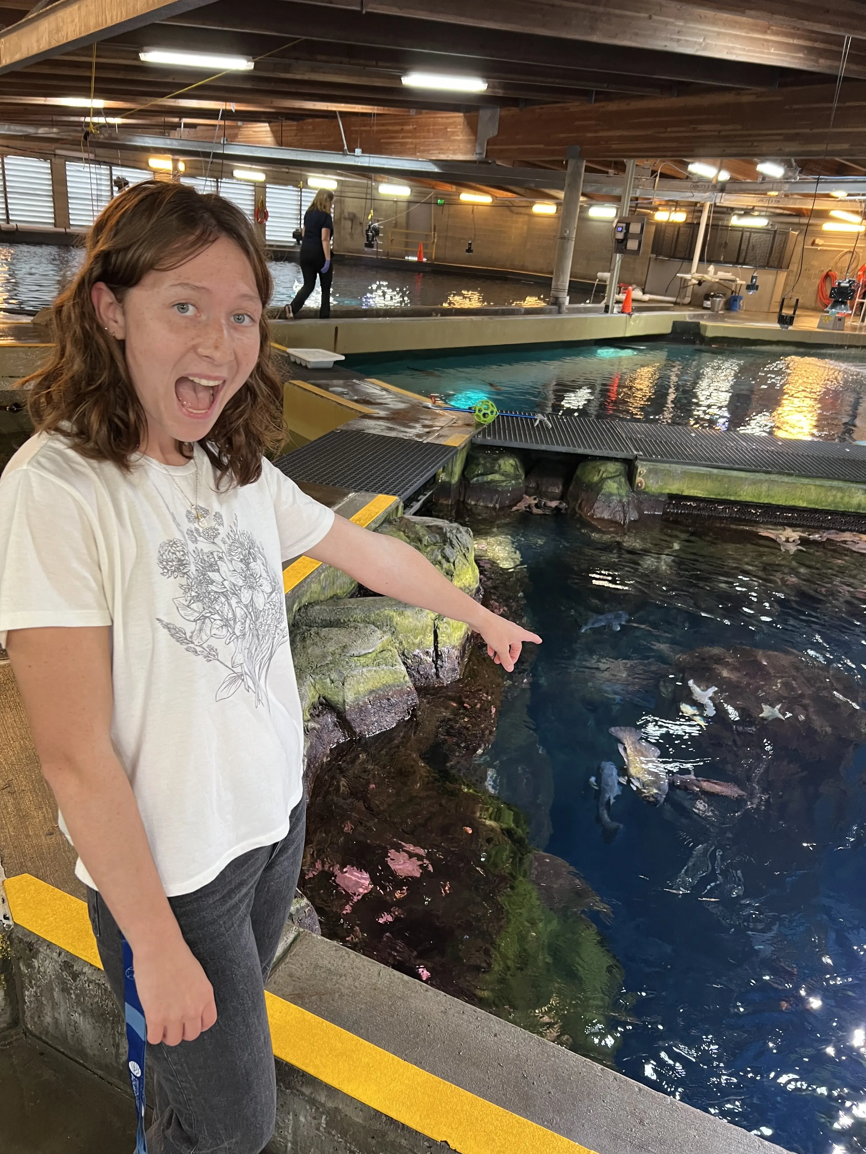 A person stands beside a large tank of water while pointing and smiling.