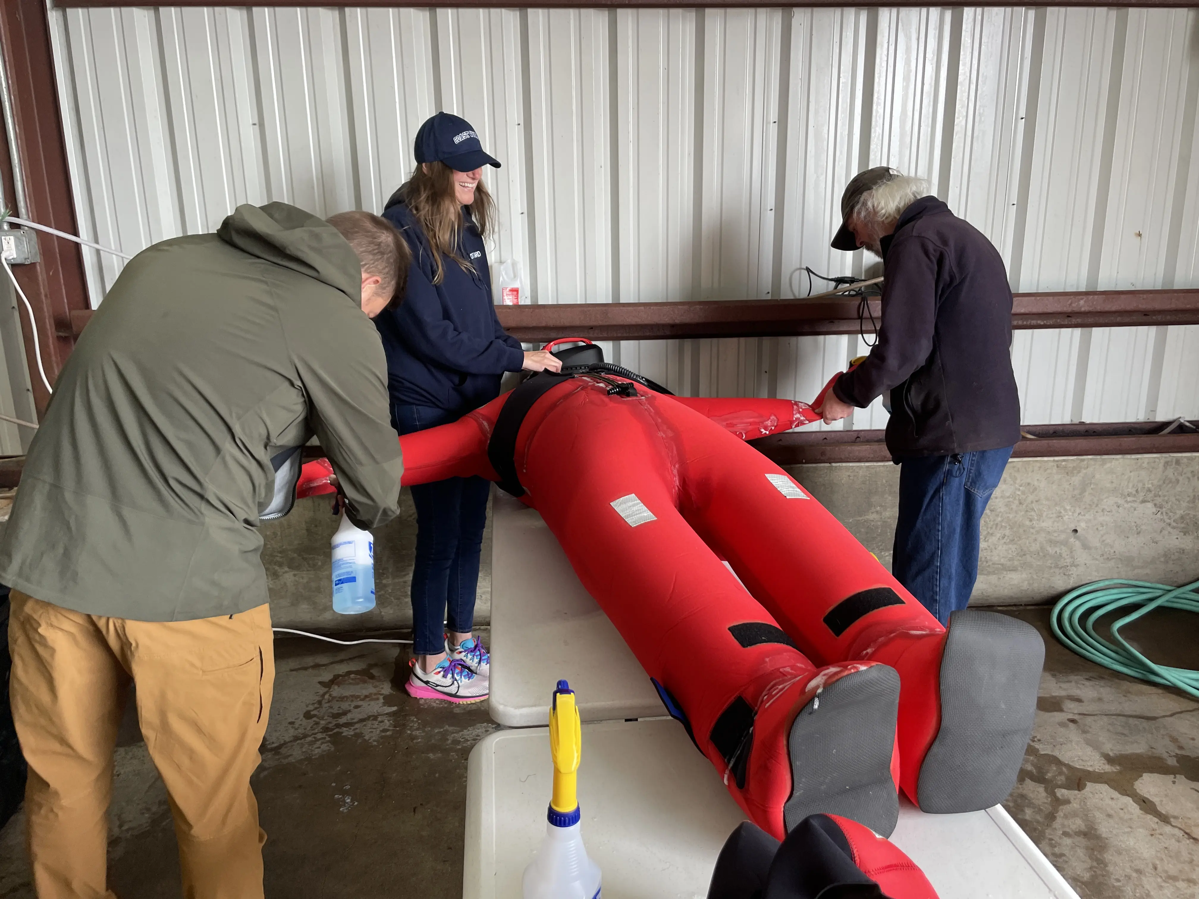 Three people stand around an immersion suit filling it with air.