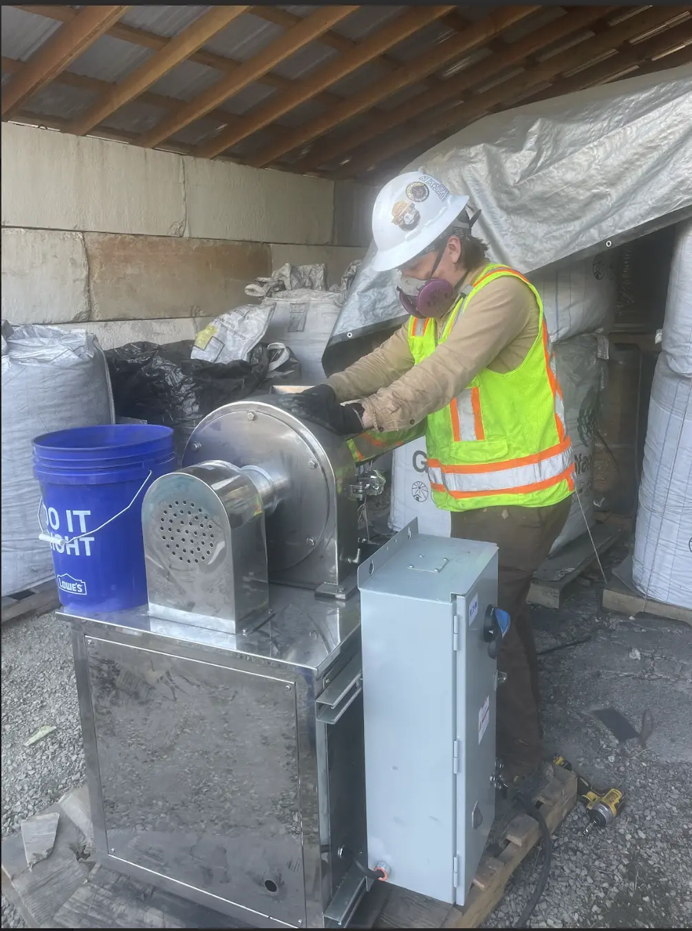 A person stands next to a concrete machine wearing bright safety vest.
