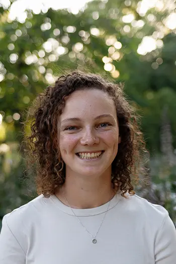 A person stands in front of green foliage and smiles at the camera. 