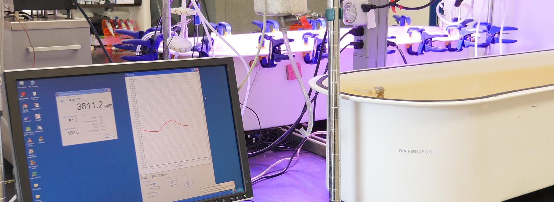 A computer sits on a desk next to a white tub under LED lights.