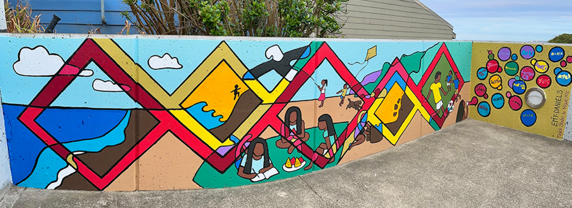A colorful mural with blue sky and a tree behind it.