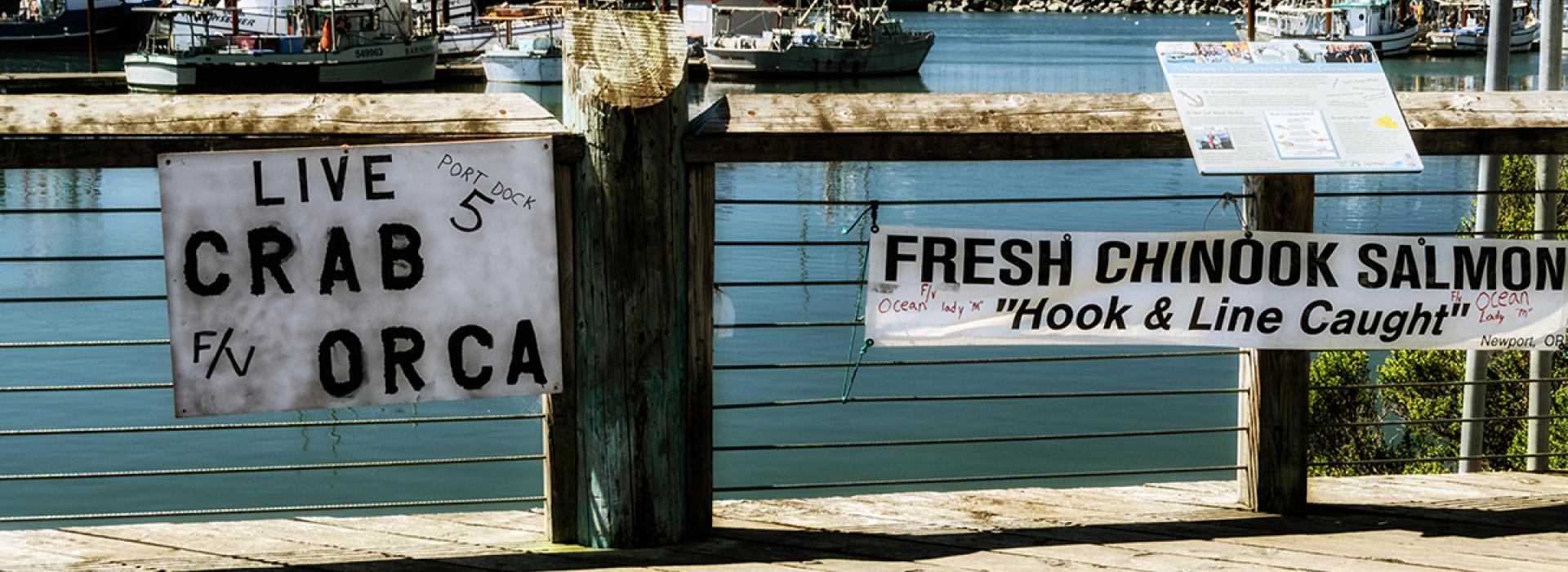 Photo of signs advertising fresh-caught crab and Chinook salmon on a dock in Newport, Oregon.
