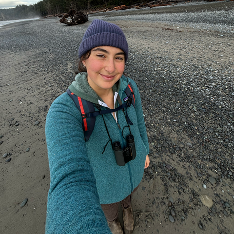 A person stands on a beach and smiles.