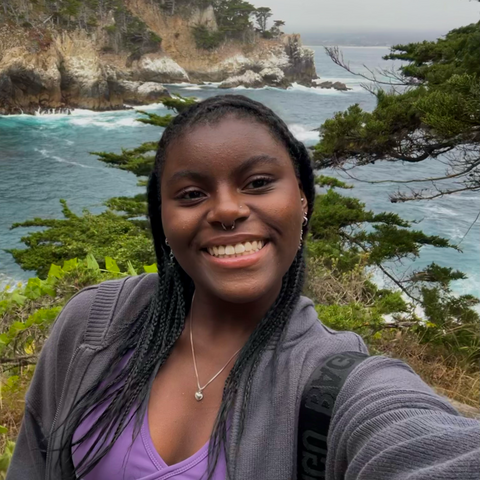 A person standing in front of a beach smiles.