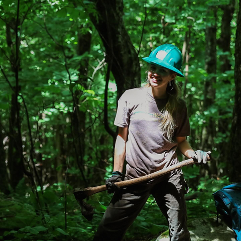 A person wearing a hard hat and holding an axe smiles.