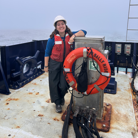 A person standing on a boat by a life ring smiles.
