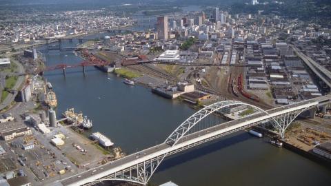 An aerial view of Portland, Oregon and the Willamette River running through it. The Fremont Bridge is in the foreground. The city buildings and roads spread out on either side of the river.