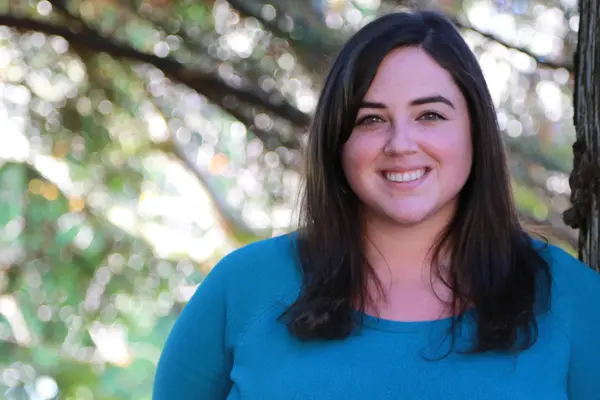 A woman smiles at the camera while leaning against a tree.