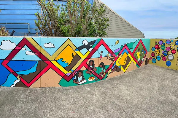 A colorful mural with blue sky and a tree behind it.