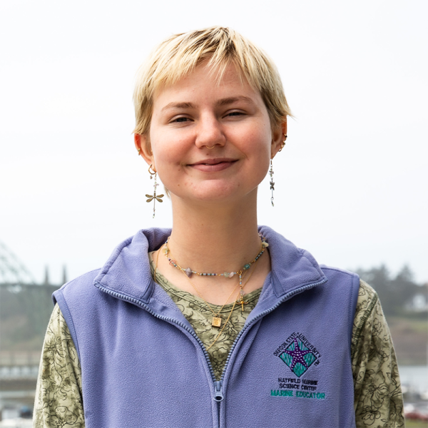 A woman wearing a purple vest smiles.