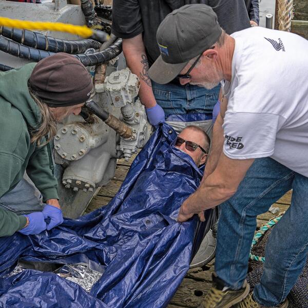A group of people life someone using a tarp.