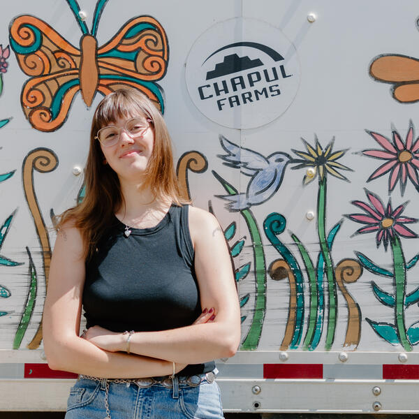 A person smiles with their arms crossed in front of a Chapul Farms truck.